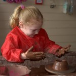 Girl on potter's wheel with clay covered hands